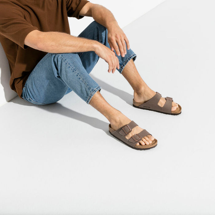 Birkenstock Arizona Birko-Flor® Nubuck sandals in taupe with dual adjustable straps and contoured cork footbed, worn by seated man.