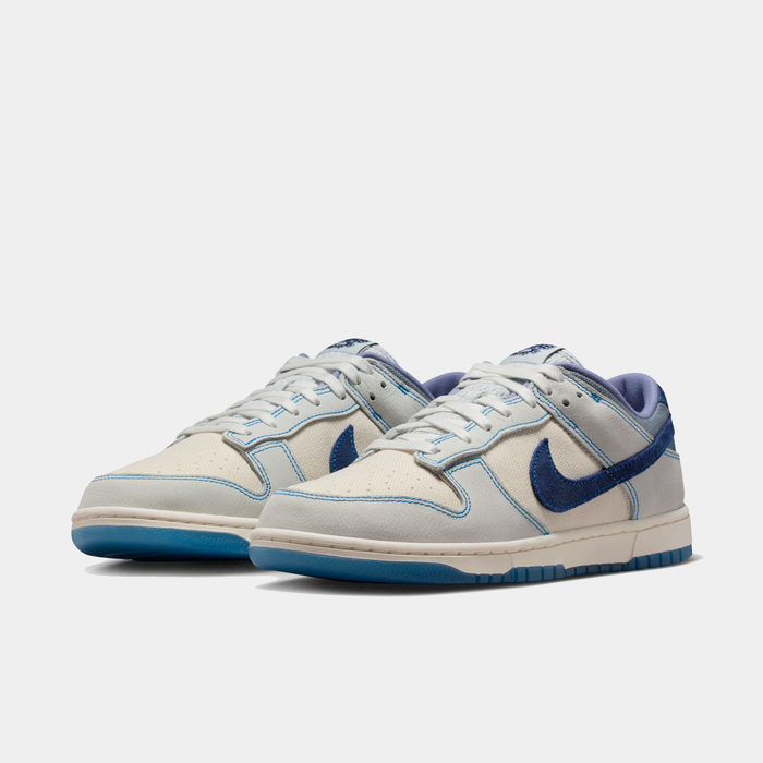 Nike Dunk Low Retro SE sneakers in cream and blue with suede Swoosh logo and perforated toe box, front angle view.