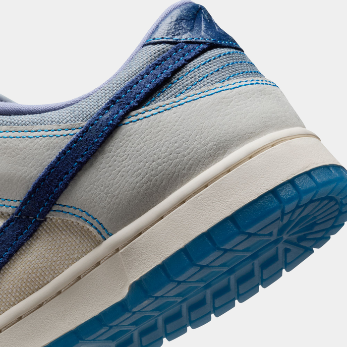Nike Dunk Low Retro SE shoes featuring a light gray leather upper, navy suede detailing, and a translucent blue rubber outsole, close-up of heel section.