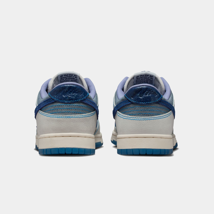Nike Dunk Low Retro SE sneakers in white and blue with textured heel details and rubber outsole, back view.