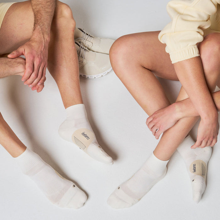 Feetures Elite Light Cushion Quarter socks in white with moisture-wicking fabric, worn by people sitting.