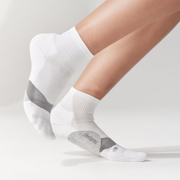 Feetures Elite Light Cushion Quarter socks in white with gray accents, worn by person standing.