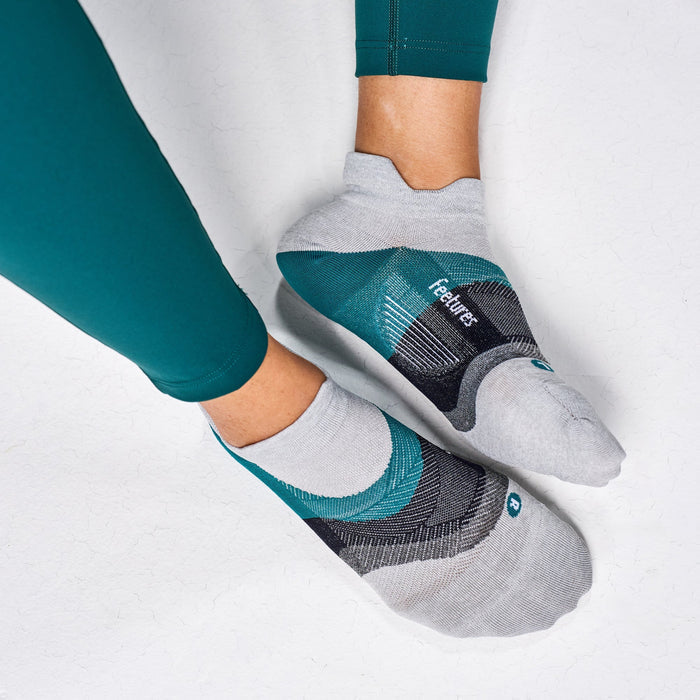 Feetures Elite Ultra Light No Show Tab socks in gray and teal with arch support, worn by person lying down.