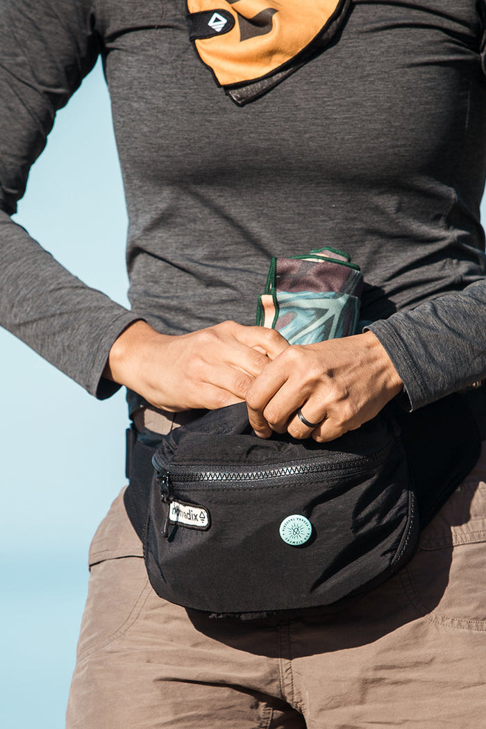 Nomadix Fanny Pack in black with zippered compartments and branded patch, worn around the waist outdoors.