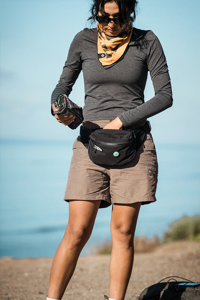 Nomadix Fanny Pack in black with zippered compartments and logo patch, worn outdoors by individual carrying gear.