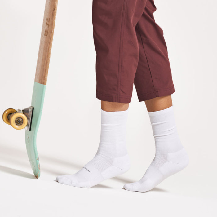 Feetures High Performance Max Cushion Crew socks in white with targeted compression and enhanced cushioning, worn by person standing.