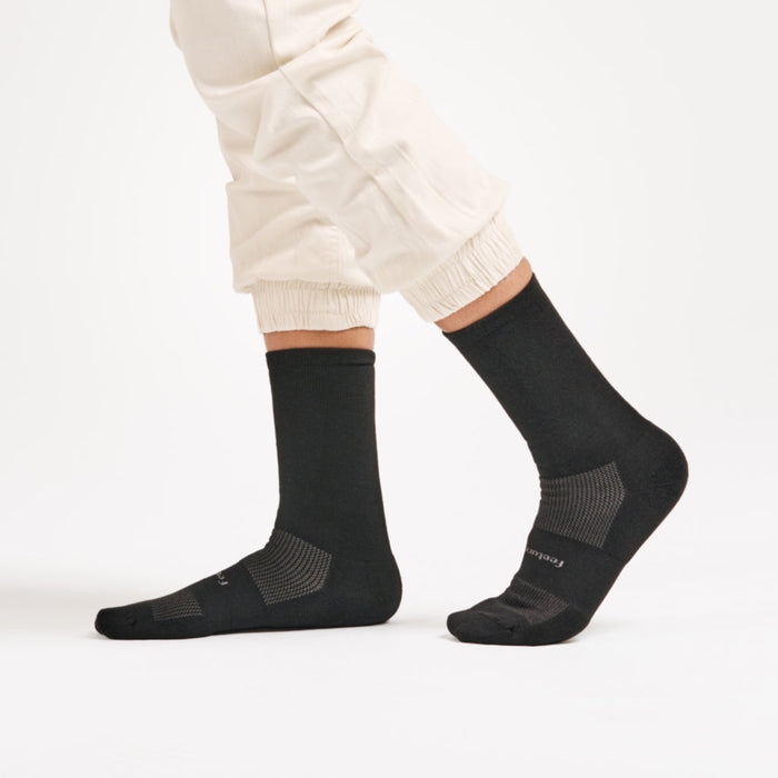 Feetures High Performance Max Cushion Crew socks in black with enhanced cushioning and mesh ventilation, worn by a person walking.