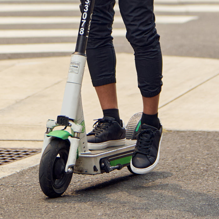 Feetures High Performance Max Cushion Quarter socks in black, offering superior comfort and cushioning, worn by a person riding a scooter.
