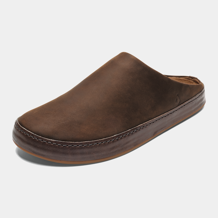 OluKai Ku'u slippers in rich brown leather with stitched detailing and a plush interior lining, angled front view.