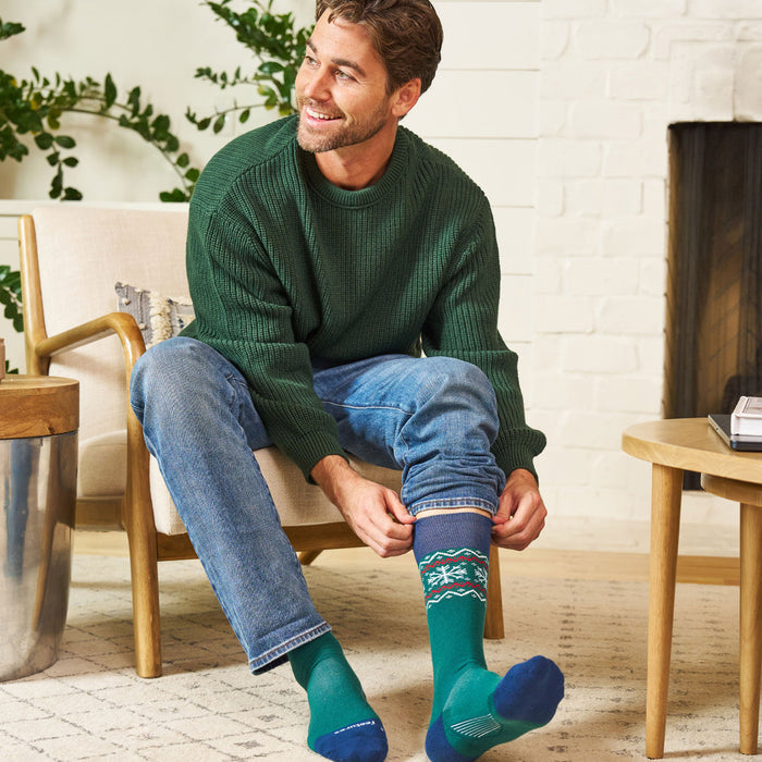 Feetures Limited Edition "Evergreen" Everyday Max Cushion Crew socks in green with festive pattern, worn in a cozy indoor setting.