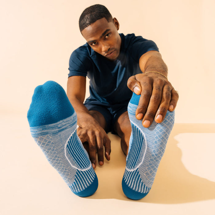 Feetures Plantar Fasciitis Relief Sock Light Cushion No Show Tab in blue and gray with targeted compression, worn during stretching