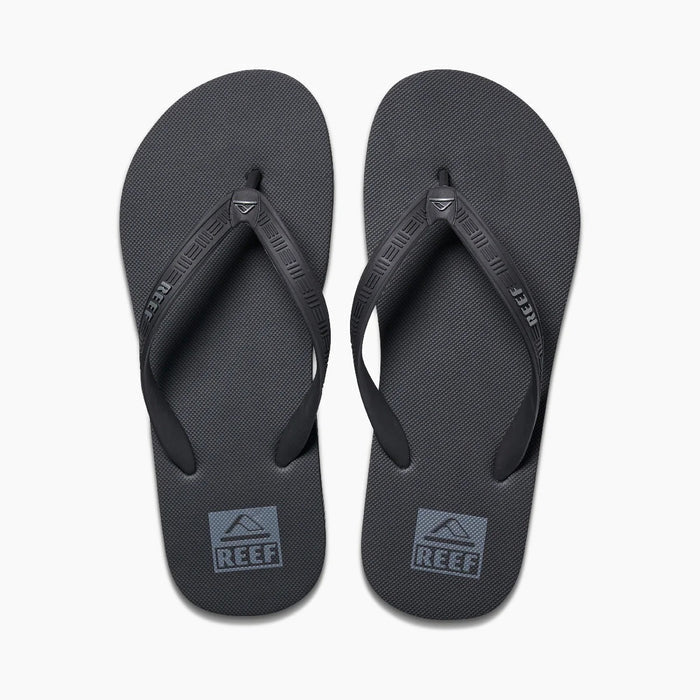 Reef Seaside flip-flops in black with textured footbed and branded straps, top view.